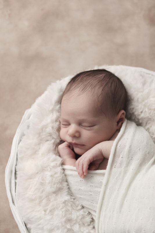 portrait minimaliste nouveau-né endormi dans panier avec fourrure crème