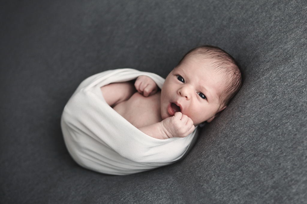 bébé éveillé et emmailloté regarde l'appareil photo