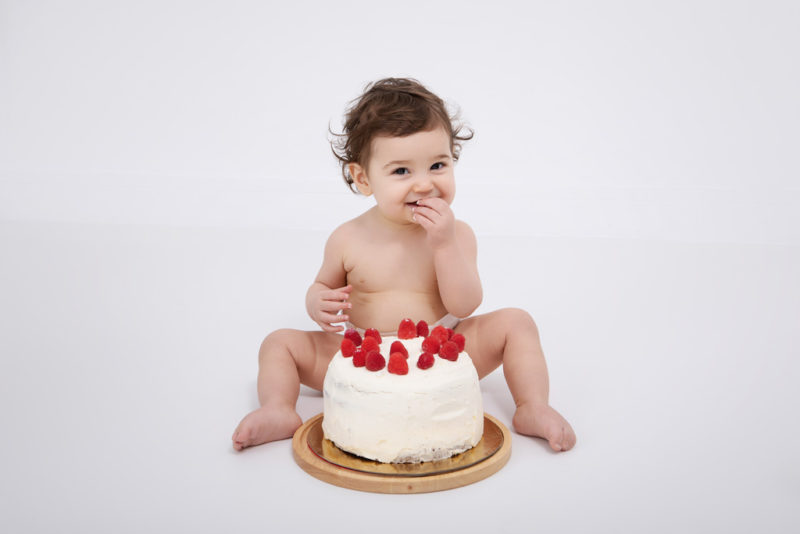 bébé qui goûte son gâteau d'anniversaire avec des framboises