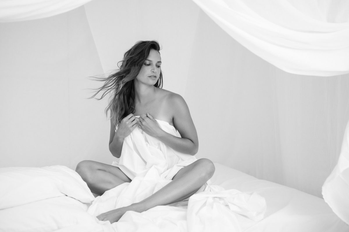 portrait noir et blanc femme dans lit à baldaquin séance photo boudoir juste un drap